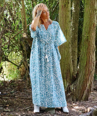 Woman standing outdoors among trees wearing an Eden bohemian printed cotton teal maxi kaftan//dress free size with a flowing boho style and intricate pattern.
