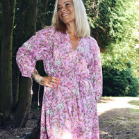 Woman standing outdoors wearing a Rosalie bohemian floral-print pink cotton maxi kaftan//dress free size with long sleeves and a relaxed fit in a natural forest setting.