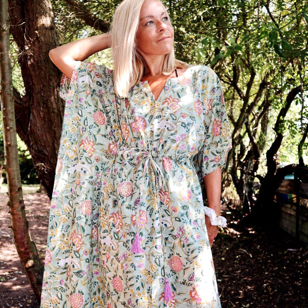 Woman wearing an Eden bohemian floral-print green cotton maxi kaftan//dress free size with loose sleeves and a drawstring waist standing outdoors among trees in soft natural light.
