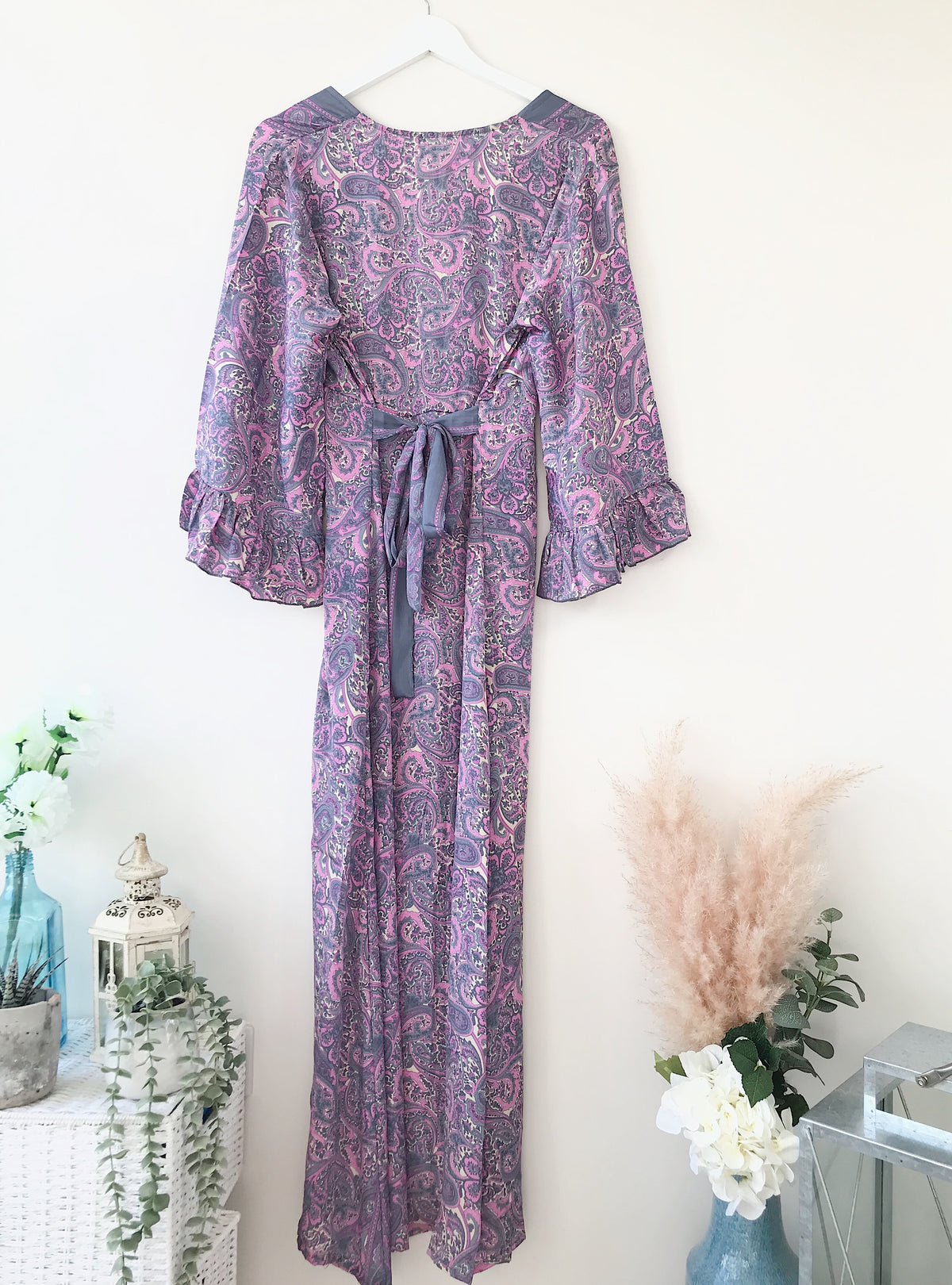 Bluebell lilac vintage-silk free-size ruffled-sleeved tie maxi dress in soft lilac paisley pattern, hanging against a light background with floral and rustic decor accents.