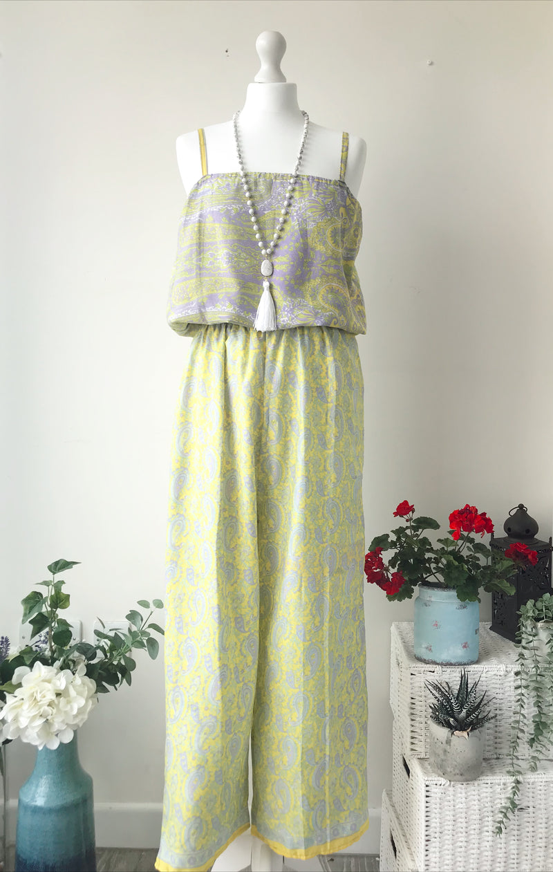 Layla yellow/lilac paisley-print silk jumpsuit free-size displayed on a mannequin with a beaded necklace, styled in a bright room with plants and flowers.