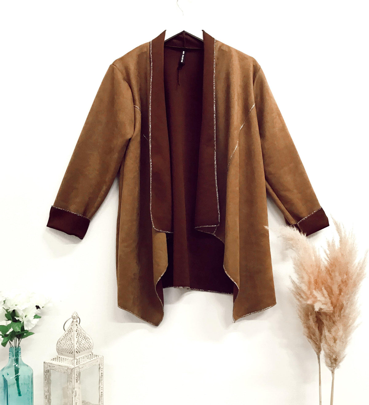 Faux-suede boho waterfall tan jacket displayed on a hanger with contrast trim, featuring a draped open front and long sleeves in a cozy boho style.